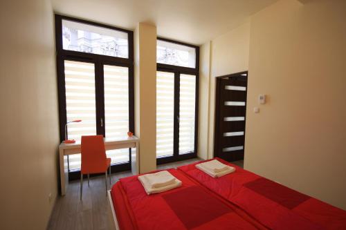 1 dormitorio con cama roja, escritorio y ventanas en Asha, en Cracovia