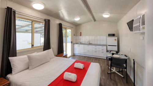 a bedroom with a large white bed and a kitchen at Emerald Tourist Park in Emerald