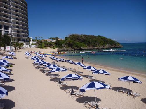 a beach with blue and white umbrellas and the ocean at Hotel Monterey Okinawa Spa & Resort in Onna