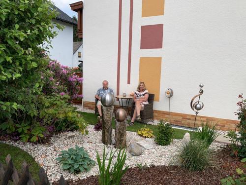 a man and woman sitting at a table in a garden at Ferienwohnungen und Gästezimmer Herrmann in Steinbach am Wald