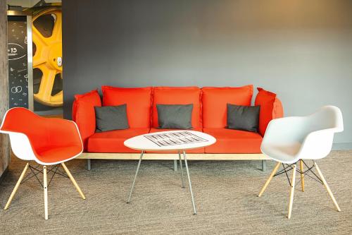 a red couch with two chairs and a table at ibis Birmingham Airport Terminal Building - NEC in Bickenhill