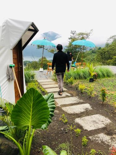 a person walking down a path with two blue umbrellas at Kubah Bali Glamping in Kintamani