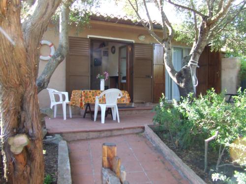 un patio con sedie bianche, tavolo e albero di Villa Chiara Villetta con giardino IUN 4807 a Porto Pollo