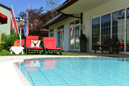 una piscina con 2 sillas rojas junto a una casa en Hotel Jagdhof, en Riezlern