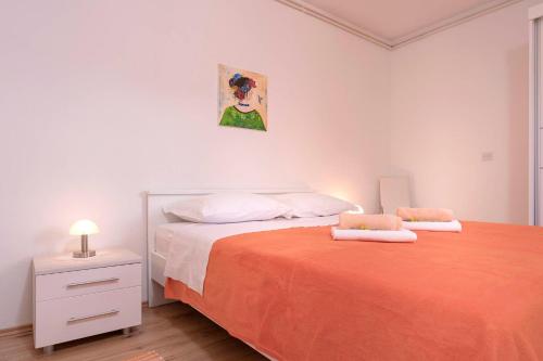 a white bedroom with a bed with an orange blanket at Apartments Ena in Vrboska