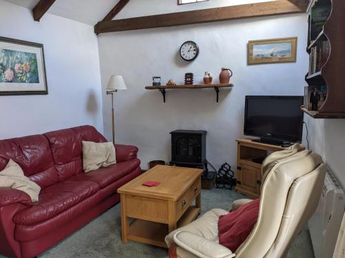 a living room with a red leather couch and a tv at The Cottage, Little Trembroath in Stithians