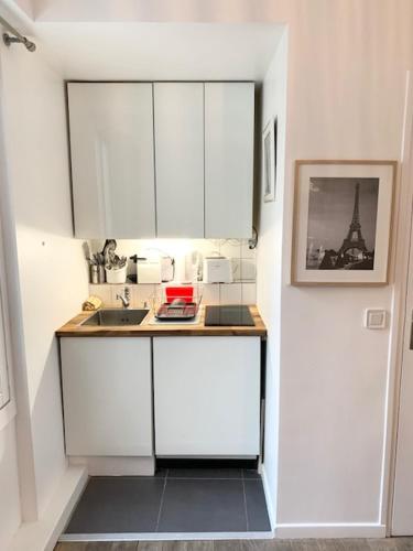 une petite cuisine avec des armoires blanches et un évier dans l'établissement Cosy Studio in Montorgueil, à Paris