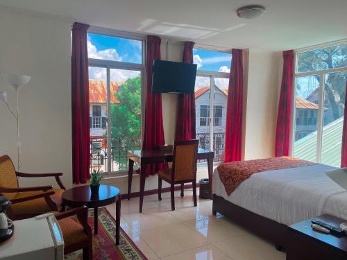 a bedroom with a bed and a desk and windows at Hotel Palacio in Paramaribo