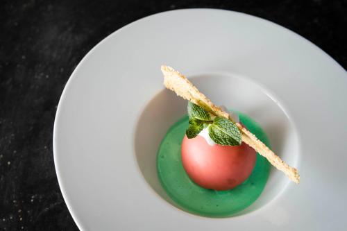 a white bowl with a green dessert with a tomato on it at Villa Tony - Small Romantic Hotel in Corvara in Badia