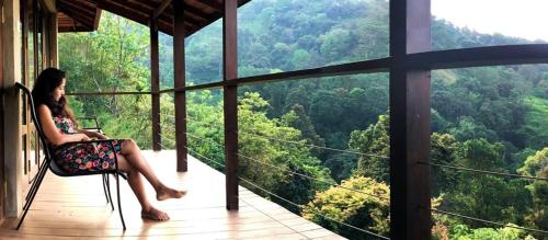 a woman sitting on a chair on a balcony looking at the forest at Benjamin Cottage Haputale in Haputale