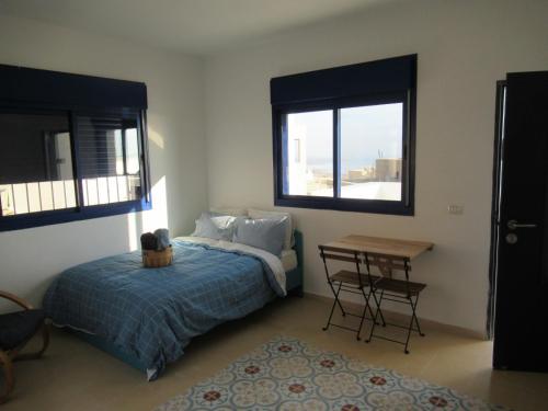 a bedroom with a bed and a table and two windows at Unique&Warmy place in the Dead Sea in Ovnat