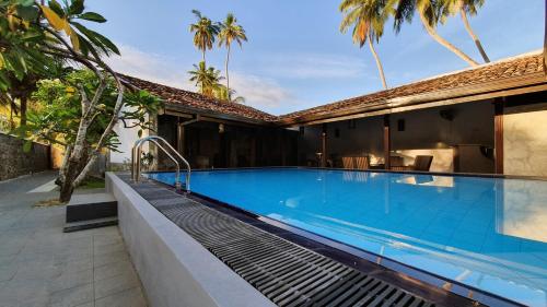 a swimming pool next to a house with palm trees at Anama by Queens Mount in Tangalle