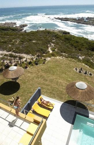 a woman sitting on a balcony with a view of the ocean at Crayfish Lodge Sea & Country Guest House in Gansbaai