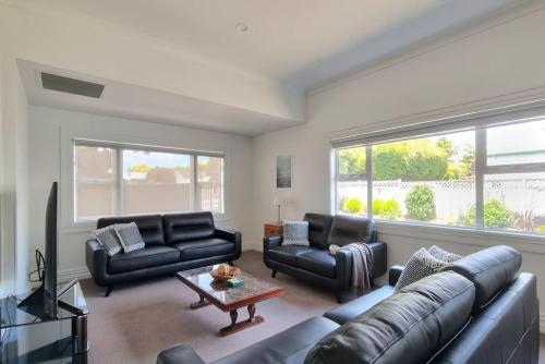 a living room with black leather couches and a tv at Central Auckland 5-Bedroom Villa with Free Parking in Auckland