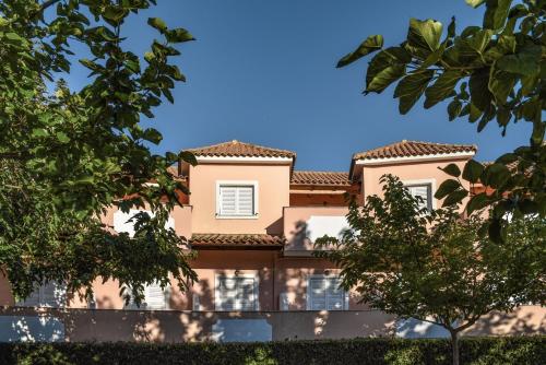 a pink building with trees in front of it at Ecoresort Hotel Zefyros in Ayios Kirikos