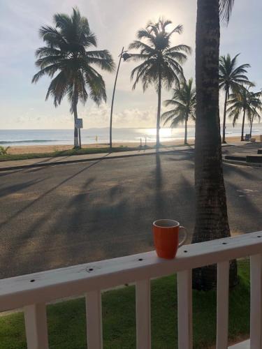 an orange coffee cup sitting on a railing overlooking the beach at Luquillo Sunrise Beach Inn in Luquillo