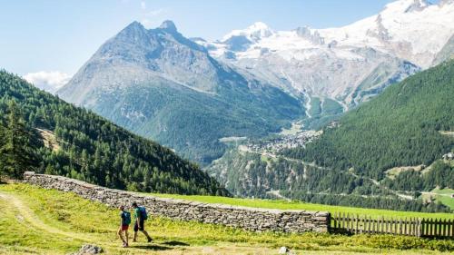 two people walking on a hill overlooking a mountain valley at Chalet Ideal Saas-Fee in Saas-Fee
