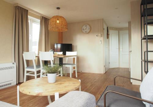 a living room with a table and chairs and a clock at Chaletparc Krabbenkreek Zeeland - Chalet 154 in Sint Annaland