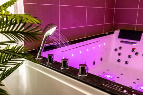 La salle de bains est pourvue d'une baignoire avec éclairage violet. dans l'établissement LoveSparadise - Suite L'élixir, à Chessy
