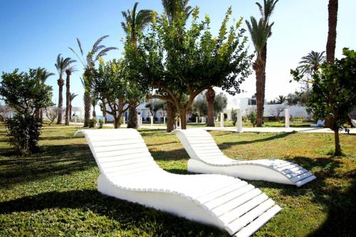 two white benches in a park with palm trees at Hotel Best Beach- Family Only in Chott Meriem
