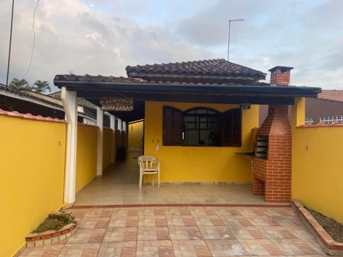une maison jaune avec une chaise sur une terrasse dans l'établissement Casa térrea em Caraguatatuba, à Caraguatatuba