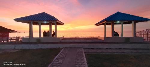 a group of people standing on a pier with a sunset at penginapan karanglaut santolo in Cilauteureun