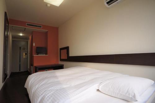 a bedroom with a white bed and a red wall at Green Rich Hotel Suizenji in Kumamoto