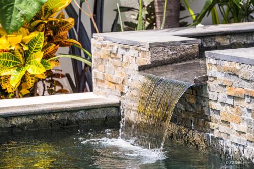 a stone water fountain in a garden with plants at LA VILLA ROSAYA - Piscine & Jacuzzi in Saint-Pierre