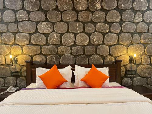 a bedroom with a bed with orange pillows and a stone wall at Casa Himalaya, Auli in Joshīmath