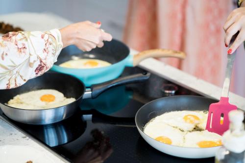 a woman cooking eggs in pans on a stove at Villa Shangri-La Zakinthos in Zakynthos Town