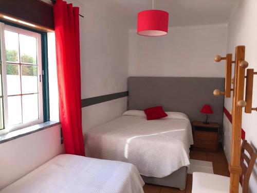 1 dormitorio con 2 camas y una ventana con cortinas rojas en Camping Villa Park Zambujeira do Mar en Zambujeira do Mar