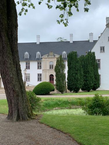 a large white house with a tree in the foreground at Schackenborg Slotskro in Tønder