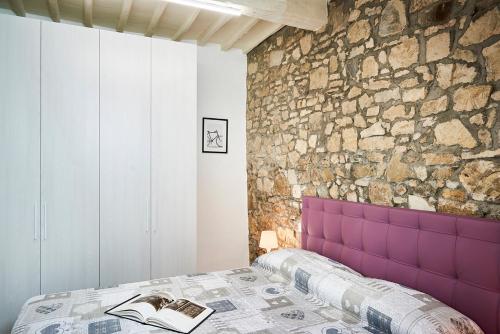 Un dormitorio con un cabecero morado y una pared de piedra. en Casa Iris Panzano in Chianti, en Pieve di Panzano