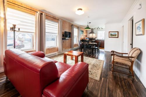 a living room with a red leather couch and a dining room at Auberge Sous les Arbres in Gaspé