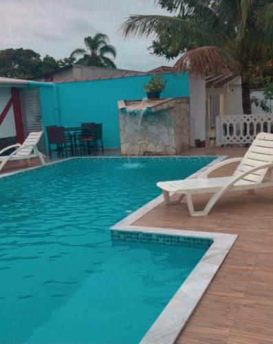 einen Pool mit weißen Stühlen und einer blauen Wand in der Unterkunft Casa para temporada e fins de semana in Itanhaém