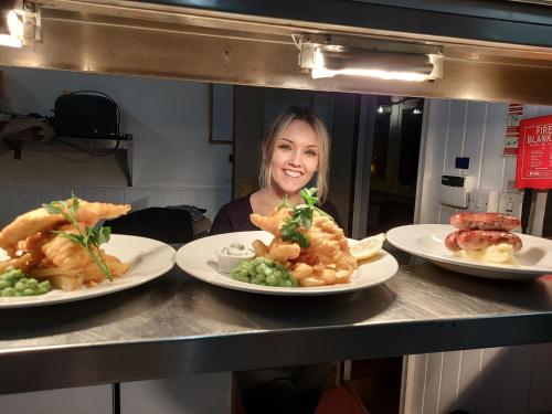 a woman behind a counter with three plates of food at Trawden Arms Community Owned Pub in Winewall