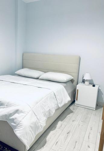 um quarto com uma cama com lençóis brancos e uma mesa lateral em Lovely Apartment at the city of Tirana em Tirana