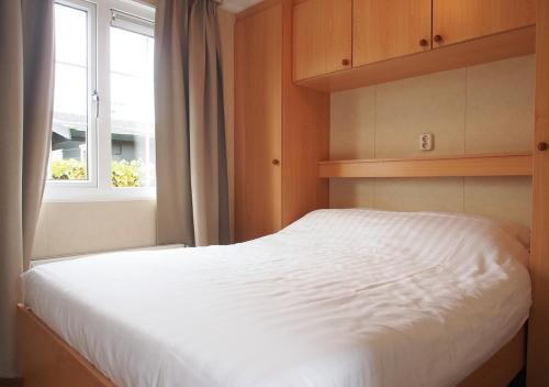 a bedroom with a white bed and a window at Chaletparc Krabbenkreek Zeeland - Chalet 152 in Sint Annaland