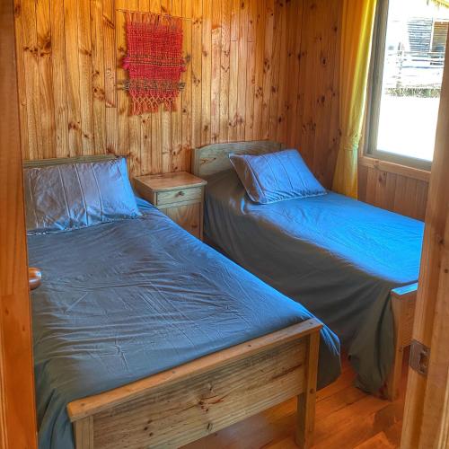 two beds in a room with wooden walls at Cabañas Refugio Las Conejas in Pelluhue