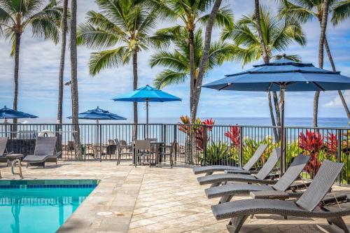 a pool with chairs and umbrellas next to the ocean at Aston Kona By The Sea in Kailua-Kona