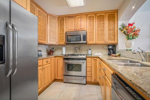 a kitchen with wooden cabinets and a stainless steel refrigerator at Aston Kona By The Sea in Kailua-Kona
