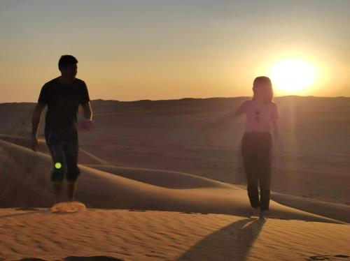 a man and a woman walking in the desert at sunset at SandGlass Camp in Bidiyah
