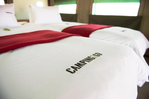dos camas blancas con un edredón con la palabra "ex-alumnos". en Etosha Safari Camping2Go, en Okaukuejo
