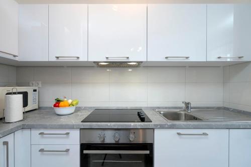 a kitchen with white cabinets and a sink and a bowl of fruit at Apartments Ena in Vrboska