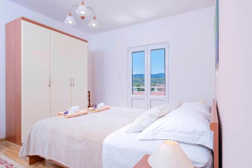 a white bedroom with a bed and a window at Apartments Ena in Vrboska