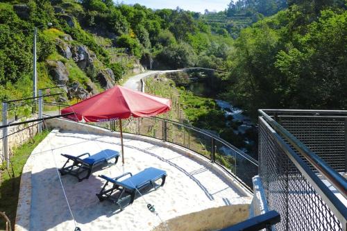 two chairs and a red umbrella on a patio with a river at Stone House by Caima River with Pool in Vale de Cambra