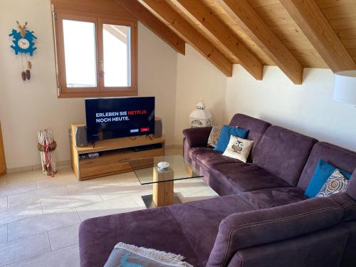uma sala de estar com um sofá roxo e uma televisão em Alpenparadies em Beatenberg