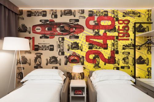 a bedroom with two beds and a wall with a picture of cars at Hotel Maranello Village in Maranello