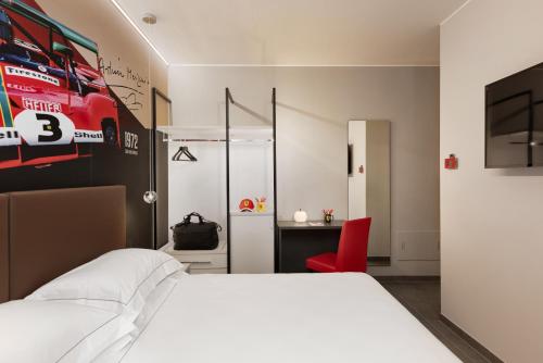 a bedroom with a white bed and a red chair at Hotel Maranello Village in Maranello