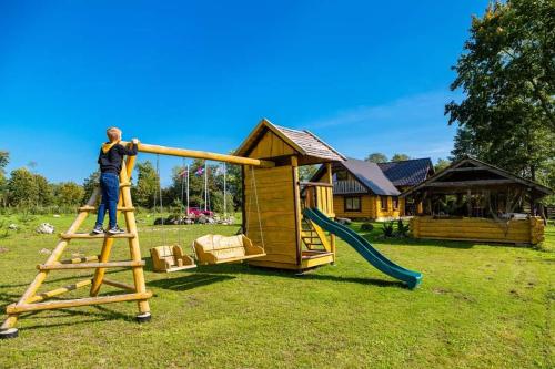 a man standing on a ladder next to a playground at Saullēkti ozolos pie Ežezera in Ezernieki